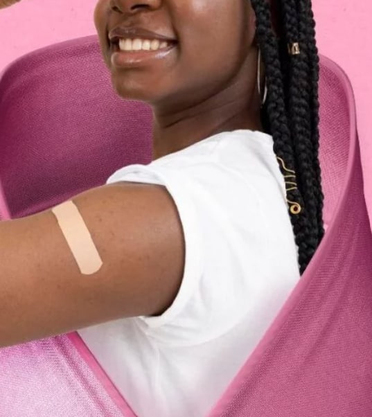 Une jeune femme souriante, un pansement au bras, enveloppée du ruban rose.